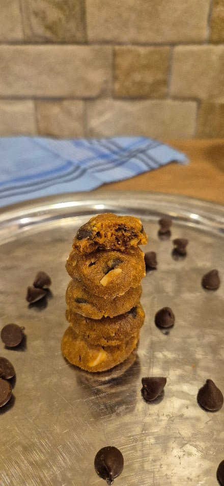 Stack of chocolate chip cookies on a metal tray with scattered cookies and a blue cloth in the background.