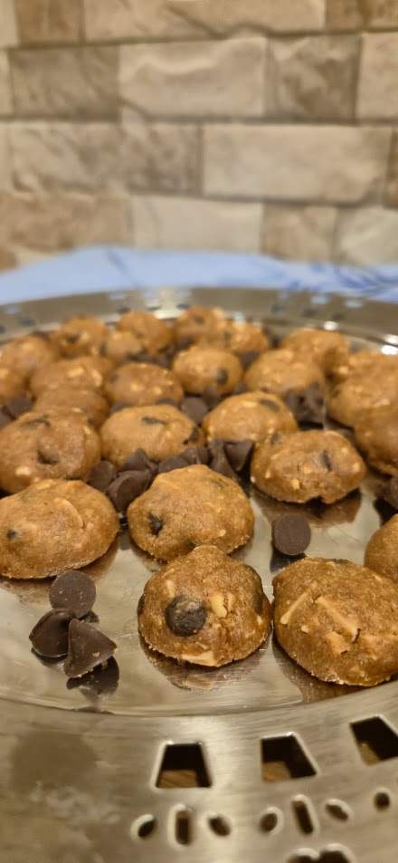 Bowl of cookie dough balls with chocolate chips on a metal tray against a stone wall background